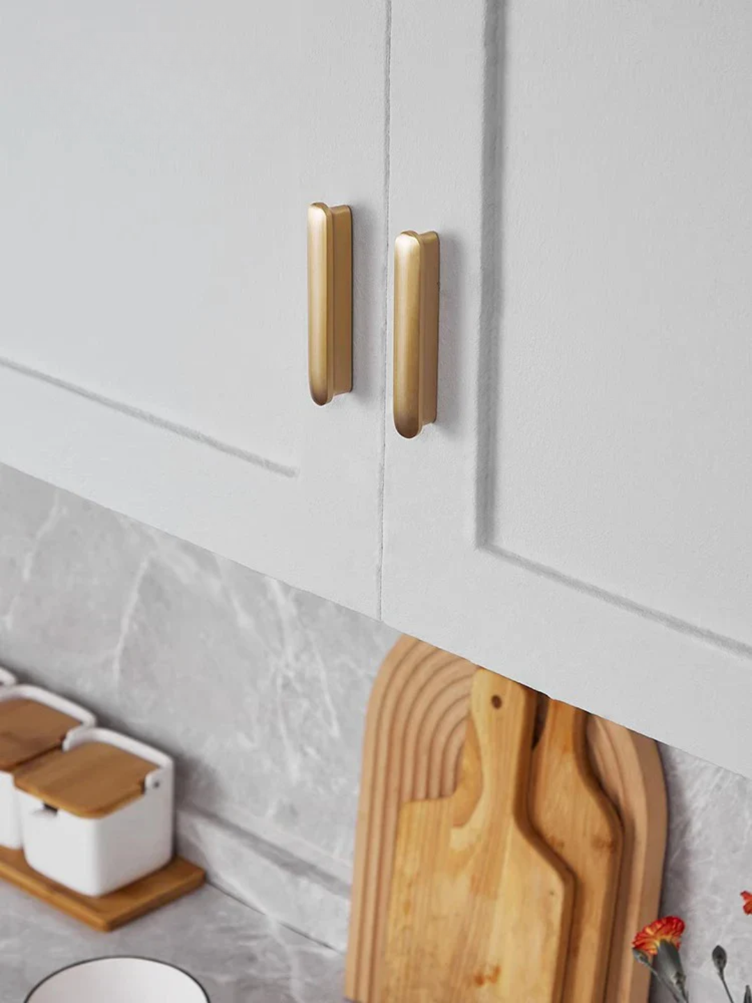 Close-up of a kitchen cabinet with gold handles and wooden cutting boards on a gray countertop.