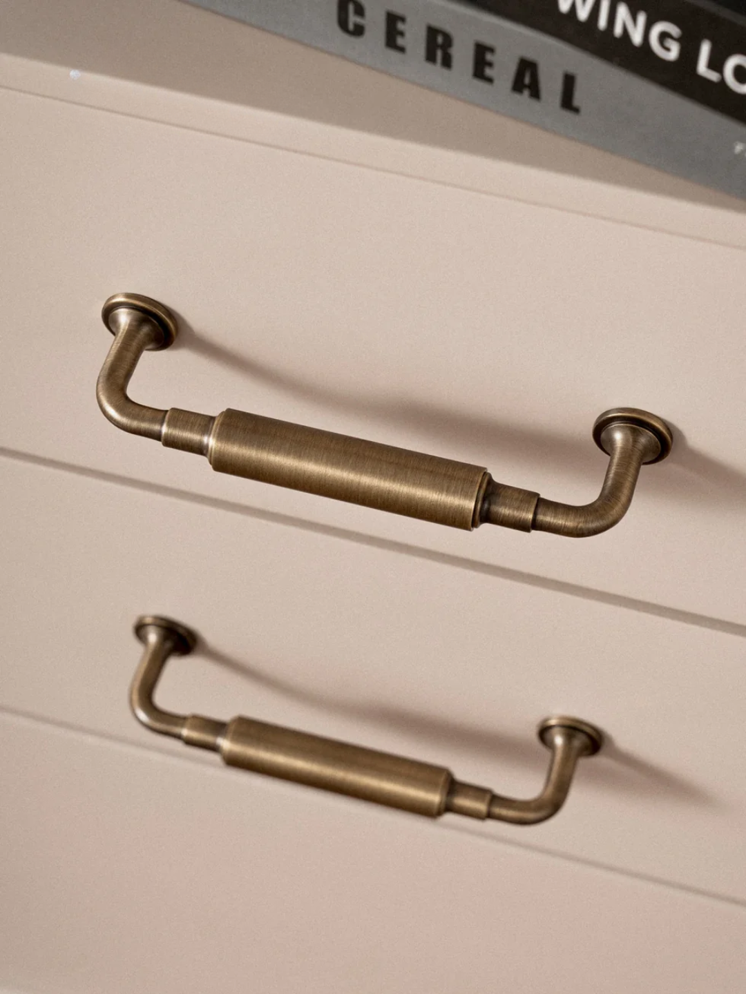 Brass cabinet handles on a wooden drawer with a cereal box in the background.