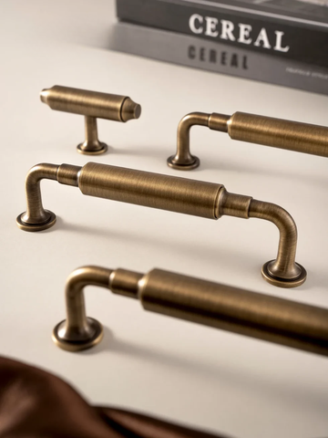 Set of brass cabinet handles on a neutral background with 'CEREAL' book in the background.