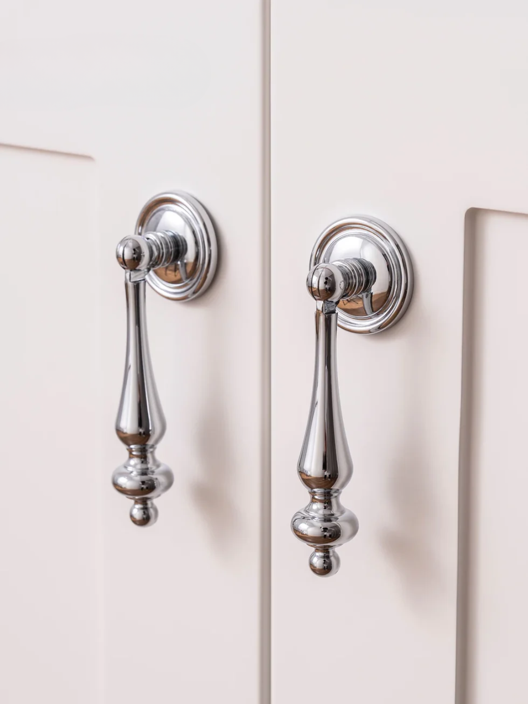 Close-up of two silver cabinet handles on a white cabinet.