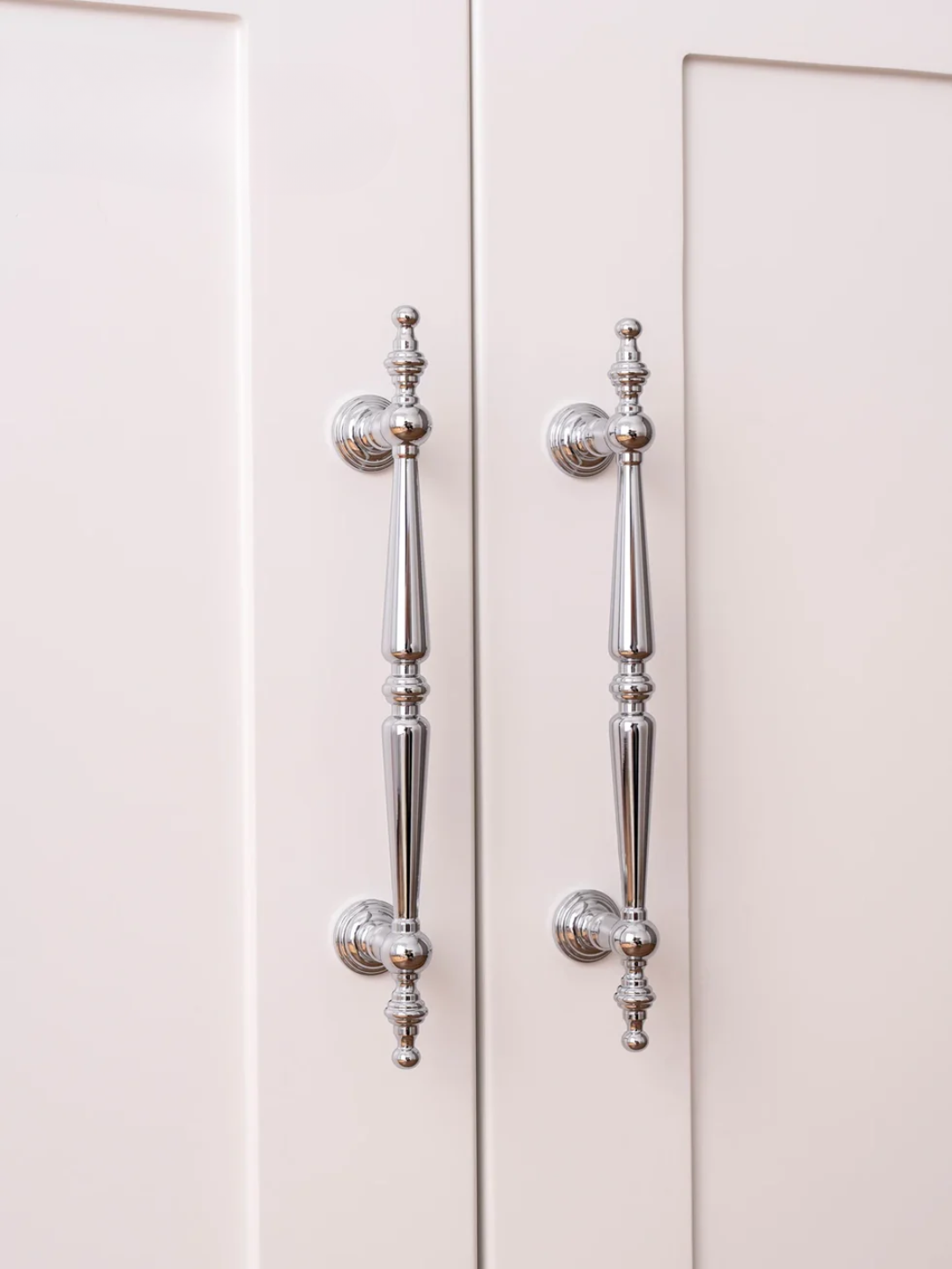 Close-up of silver cabinet handles on a light-colored cabinet door.