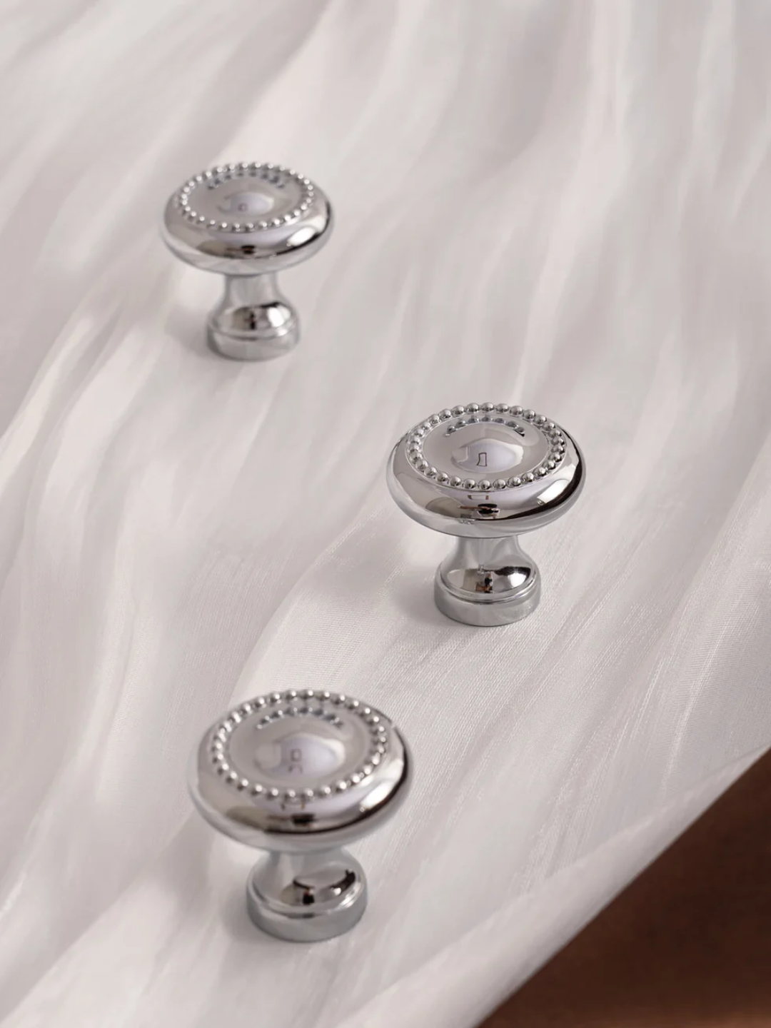 Three silver cabinet knobs on a white fabric background