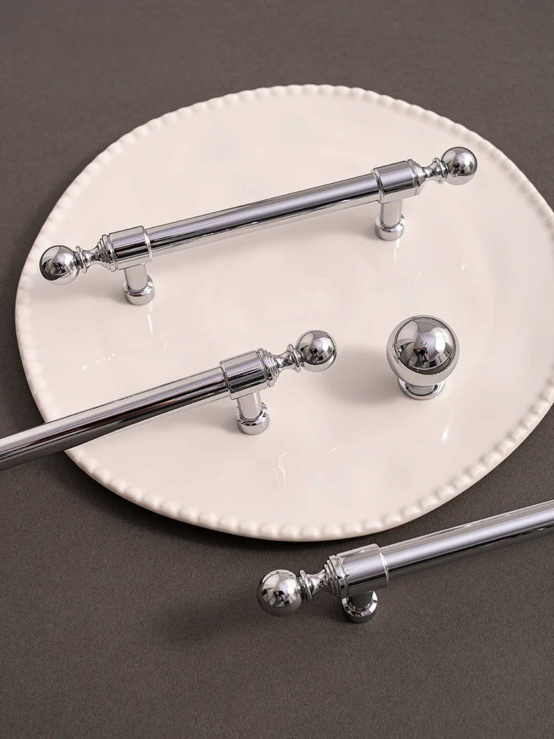 Set of silver curtain rods with decorative finials on a white plate against a dark background
