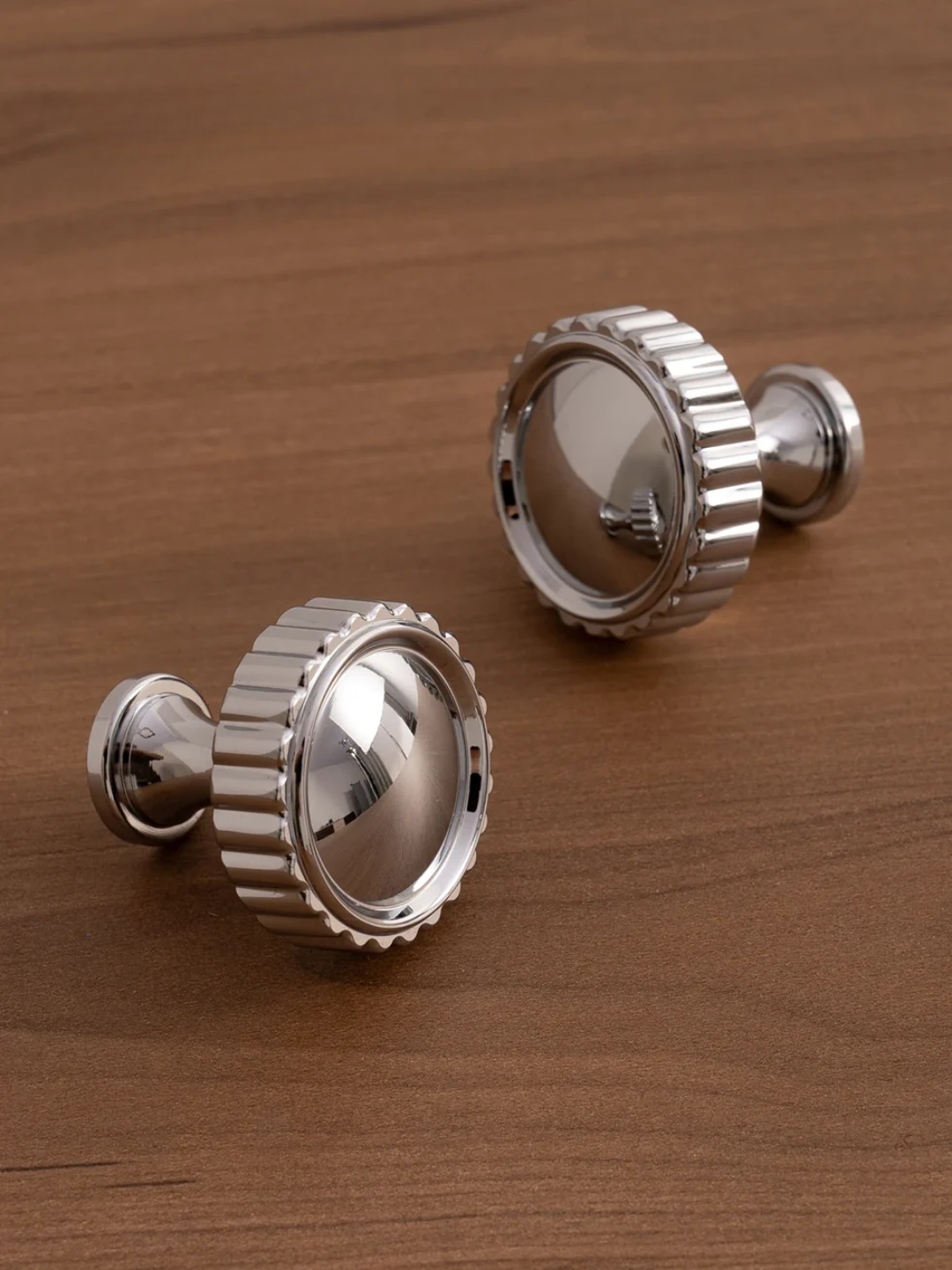 Two silver metallic knobs on a wooden surface