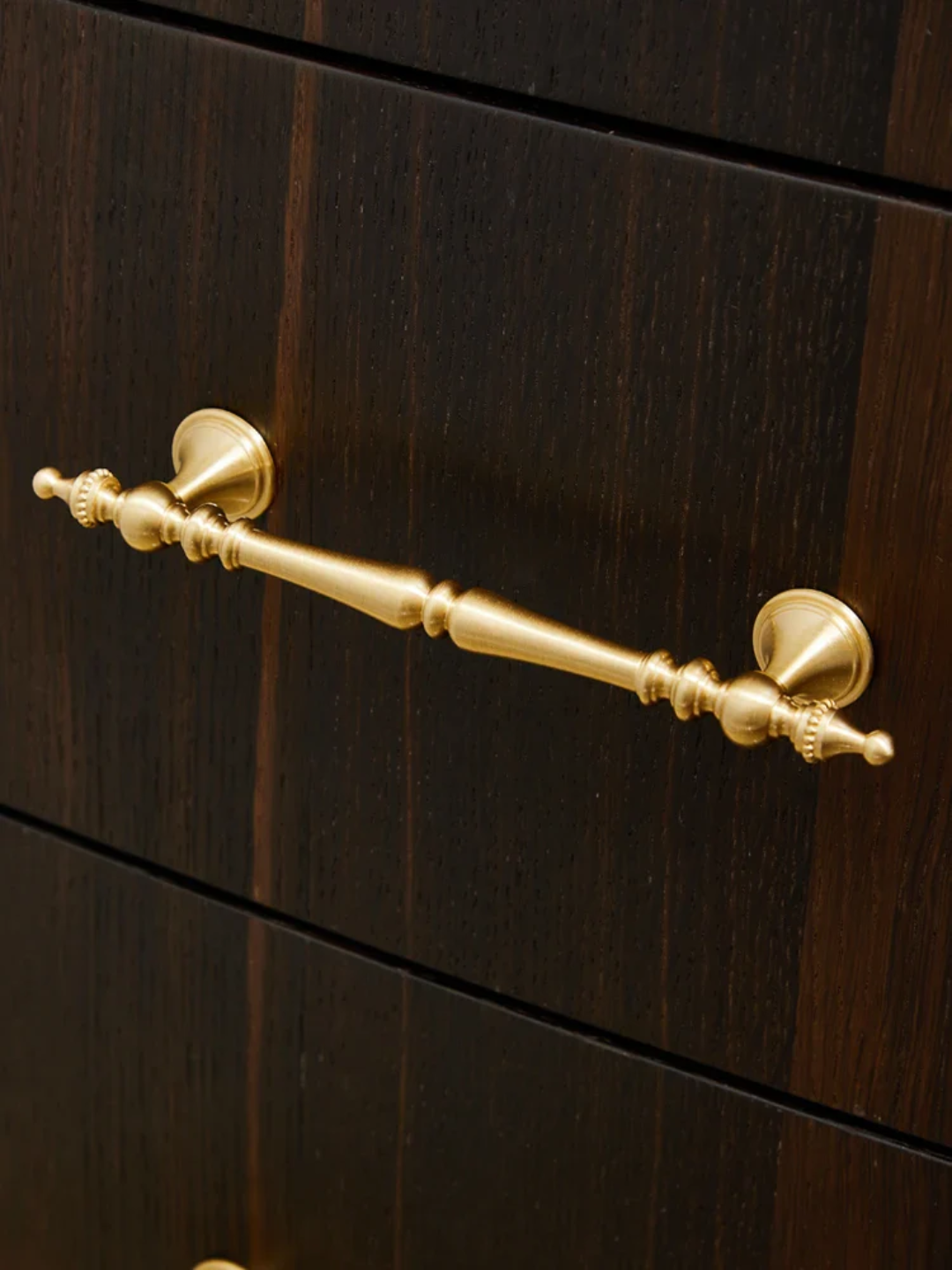 Gold cabinet handle on a dark wooden drawer