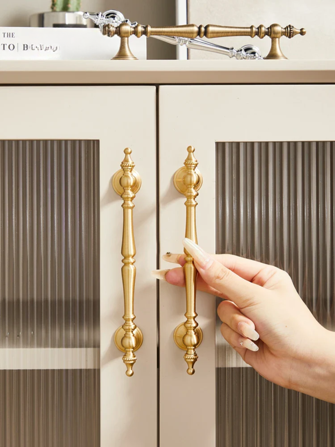 Hand opening a cabinet door with gold handles on a neutral background