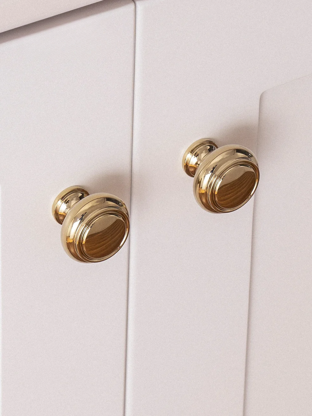 Close-up of two gold cabinet knobs on a white cabinet.