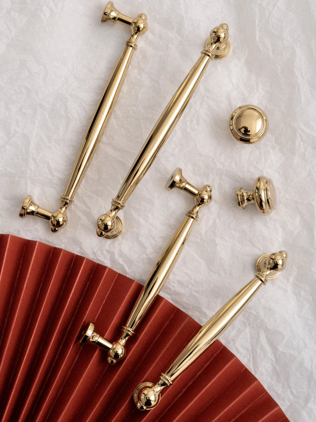 Gold hardware pieces on a textured white surface with a red fabric background