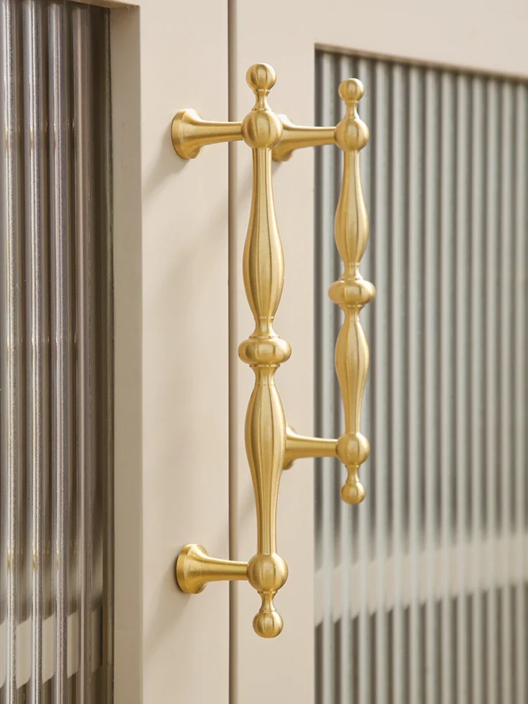 Gold cabinet handle on a beige door with striped curtains in the background