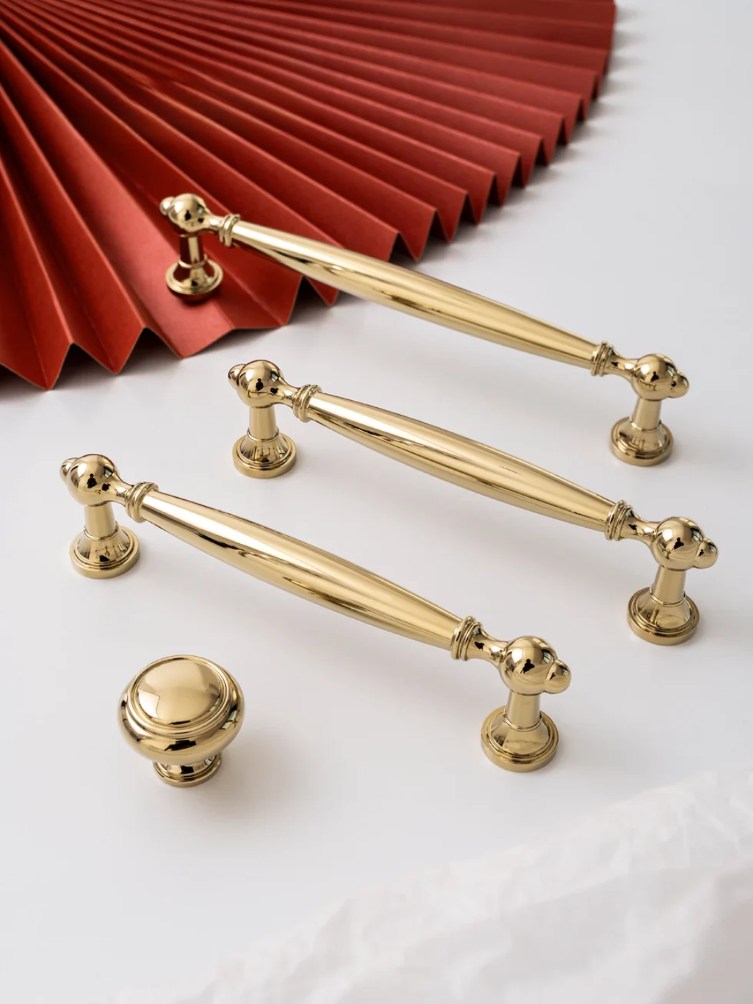 Gold cabinet handles and knobs on a white surface with a red pleated fabric background