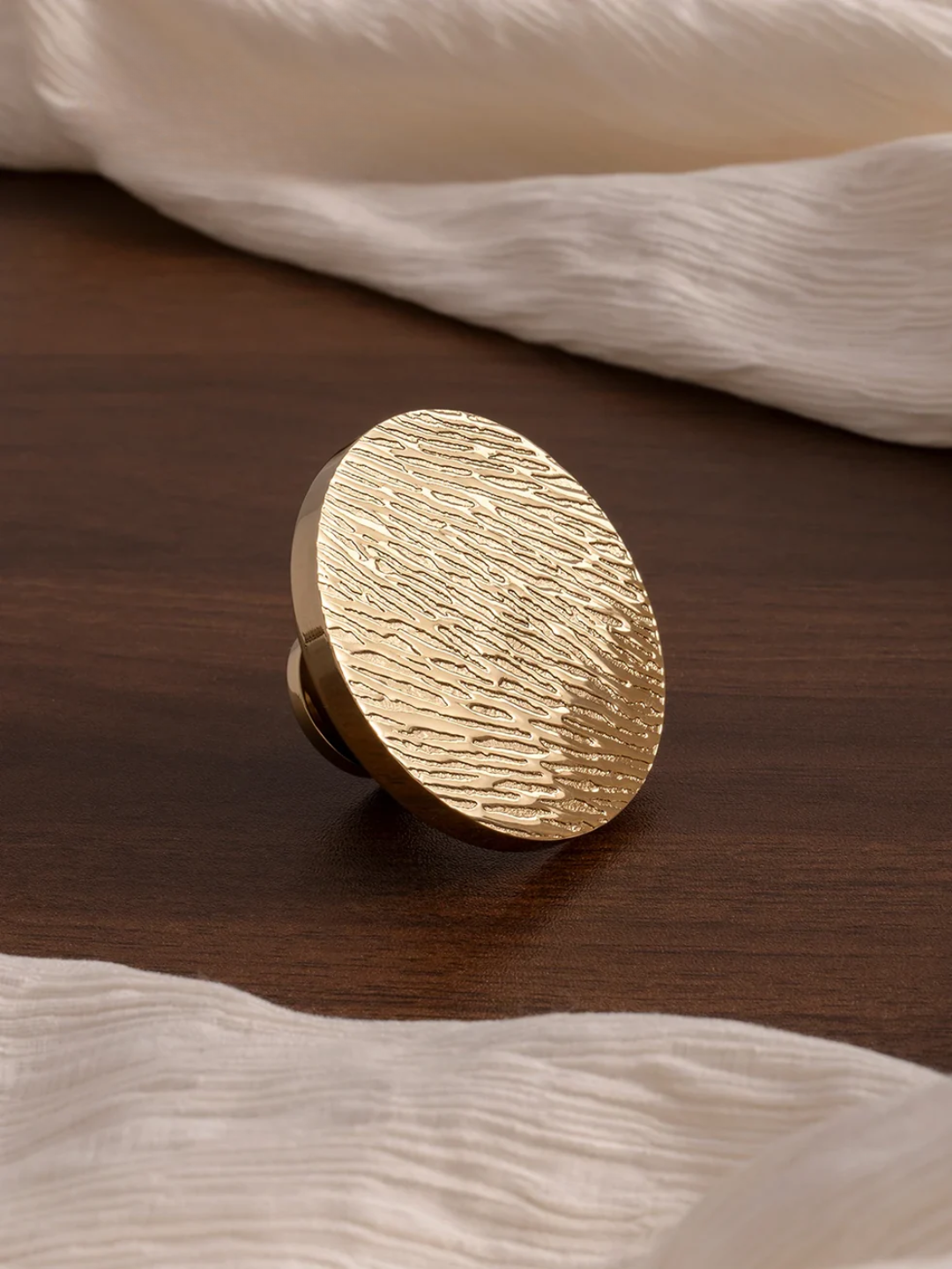 Gold textured knob on a wooden surface with white fabric in the background