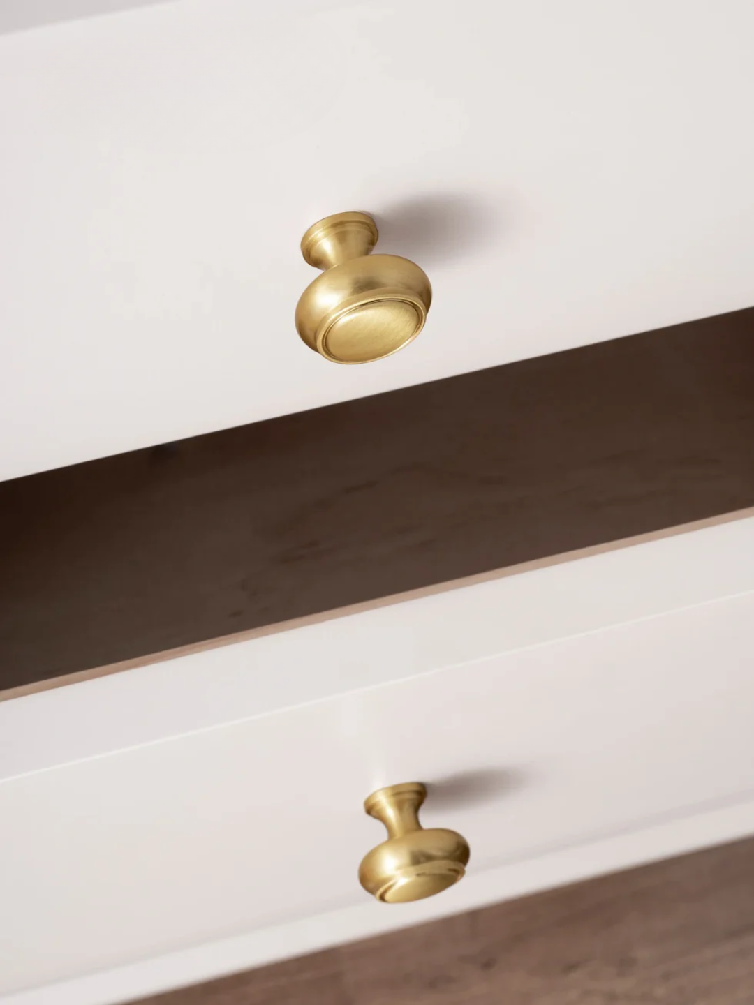 Close-up of a white cabinet with gold handles on a wooden floor.