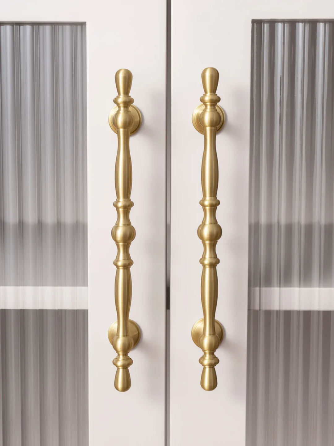 Two gold cabinet handles on a white door with a striped background