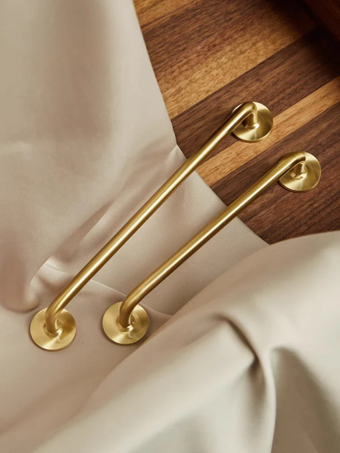 Gold handles on a wooden drawer with beige fabric background