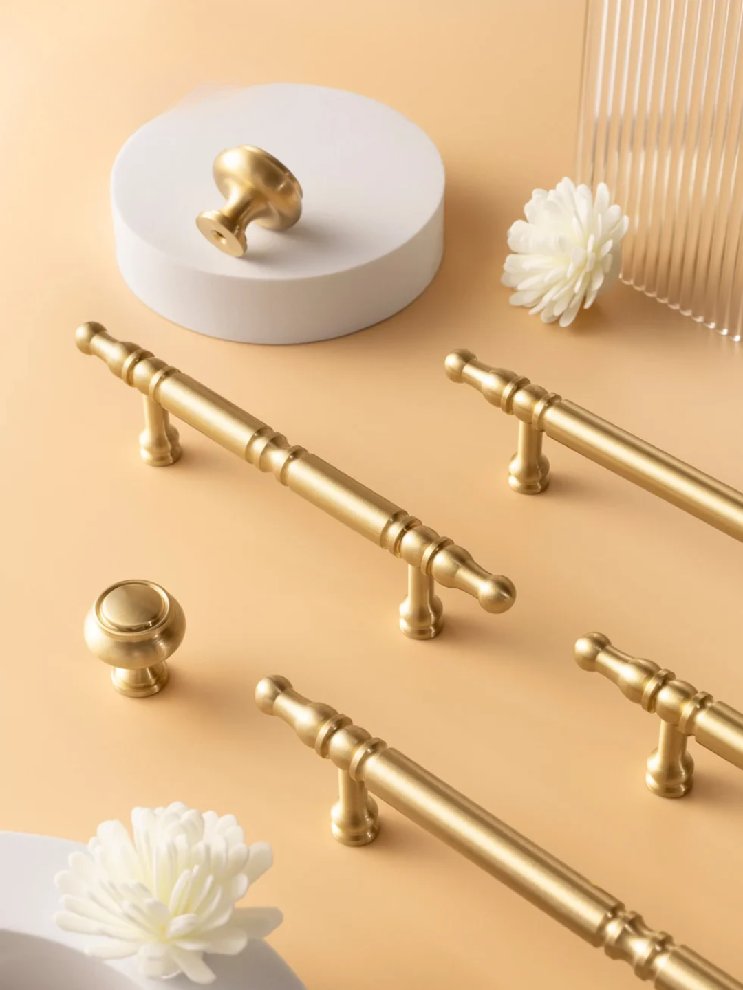 Gold cabinet handles and knobs on a beige surface with decorative elements.