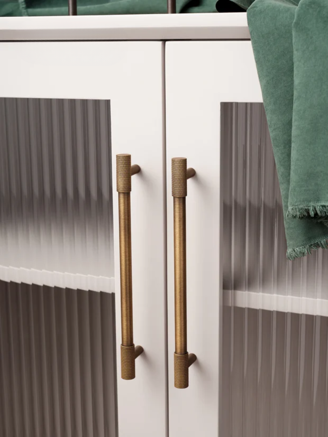 Close-up of a cabinet with gold handles and a green towel draped over it.