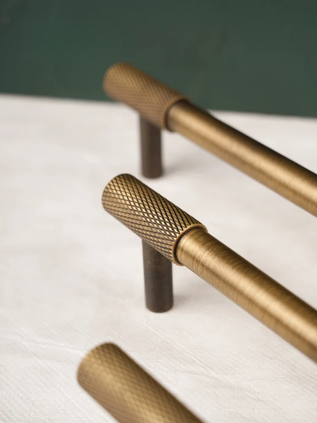 Brass cabinet handles on a white surface with a green background