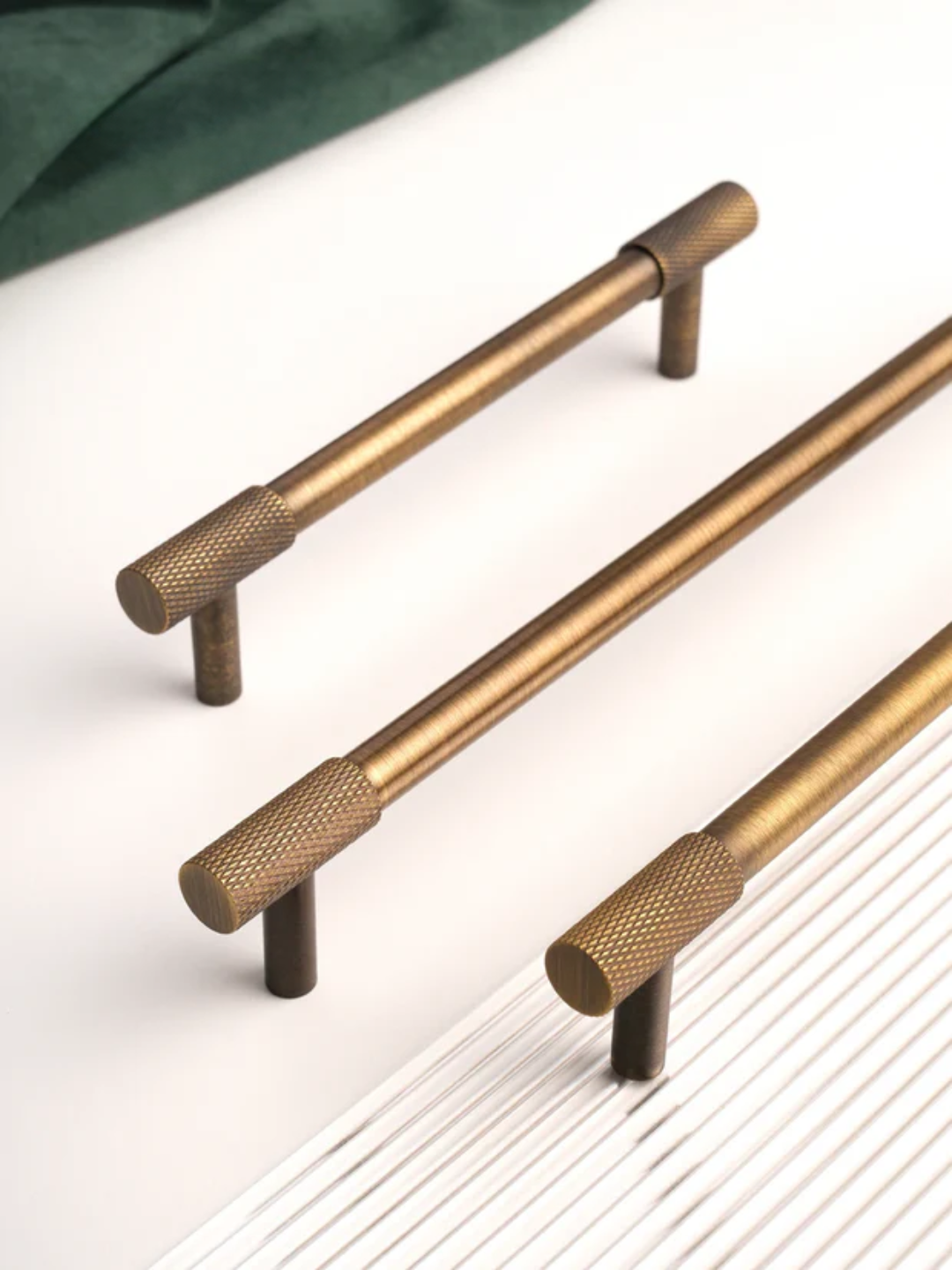 Three brass cabinet handles on a white surface with a green fabric background