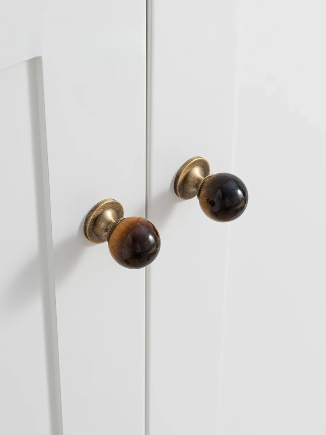Pair of door handles with brown and gold finish on a white cabinet.