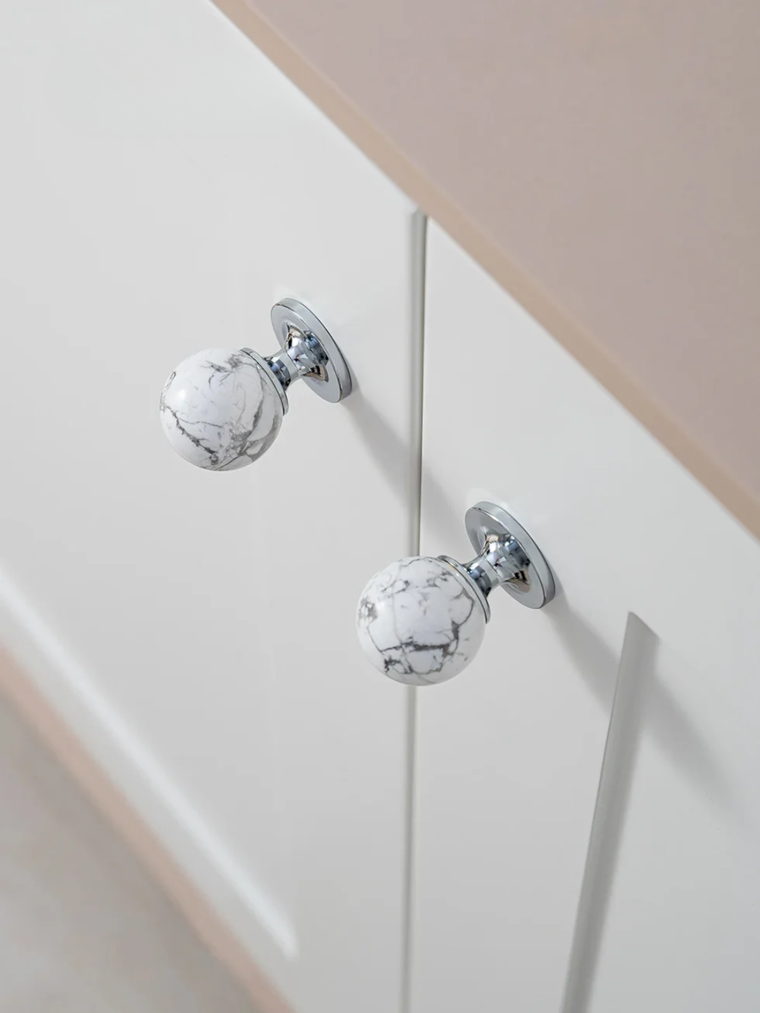 Decorative cabinet knobs with marble-like finish on a white cabinet.