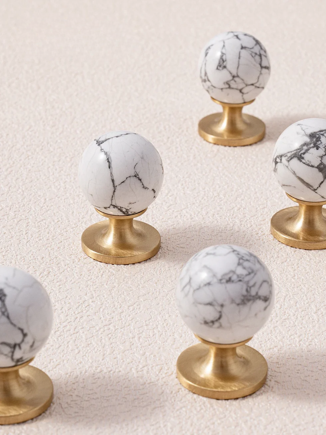 Decorative knobs with marble design and gold bases on a light background, featuring the brand 'Santaya'.