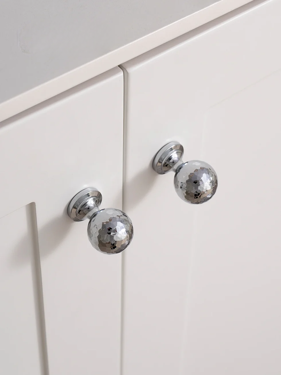 Close-up of white cabinet doors with silver metallic knobs on a light gray background