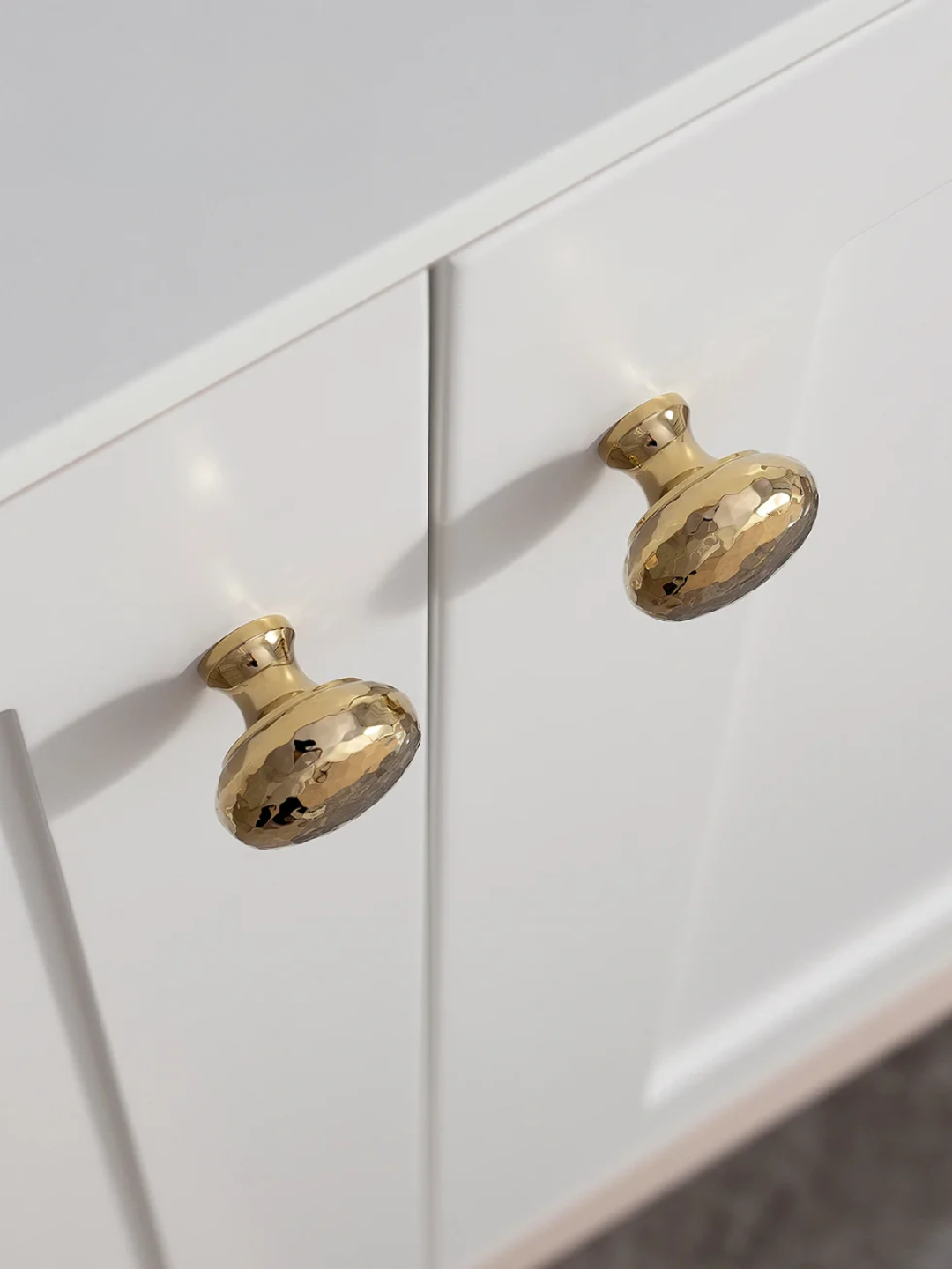 Close-up of two gold cabinet knobs on a white cabinet.