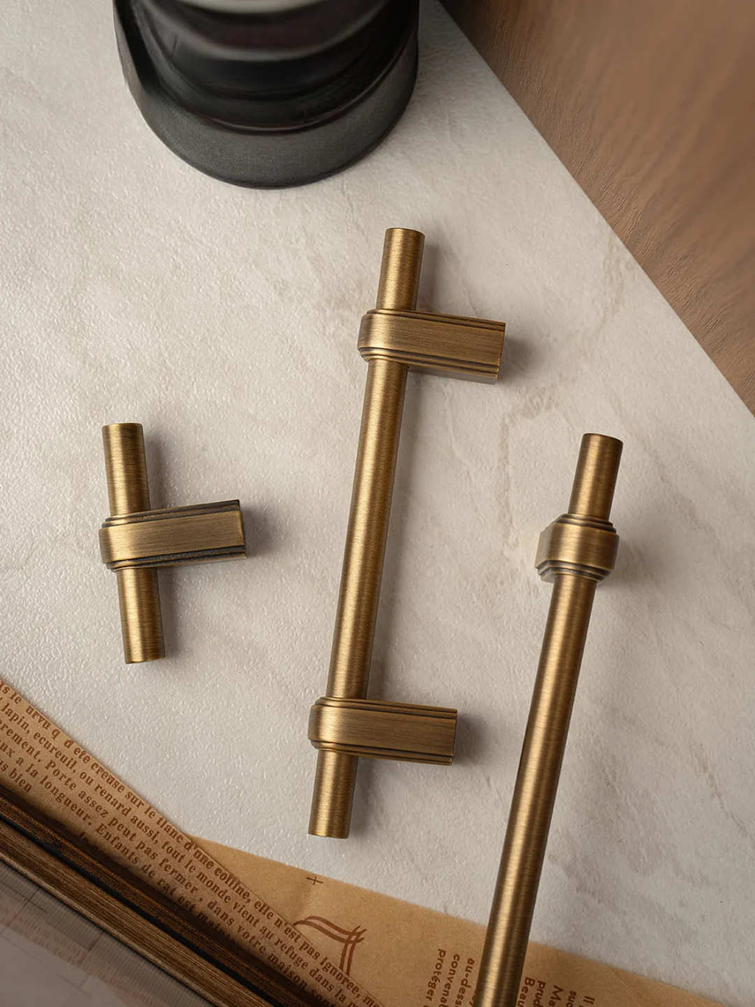 Three brass cabinet handles on a textured surface with a magazine underneath.