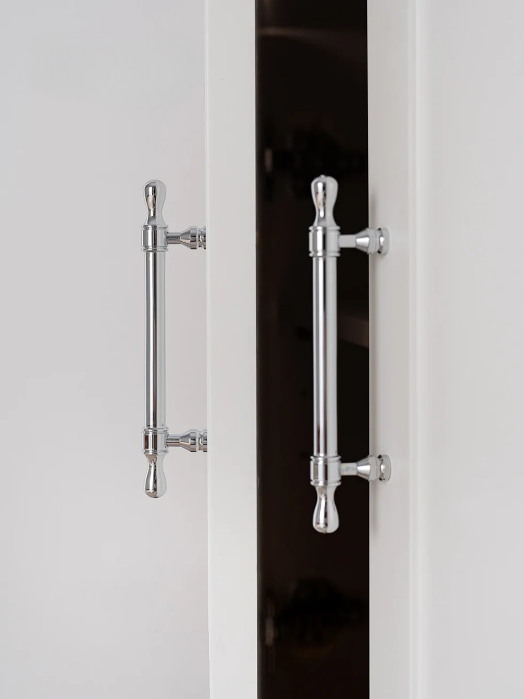 Close-up of two silver cabinet handles on a white door.