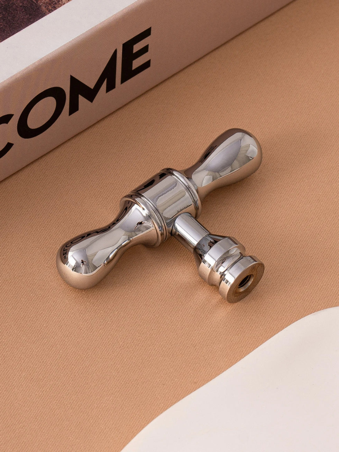 Metallic door handle on a beige surface with 'COME' text in the background