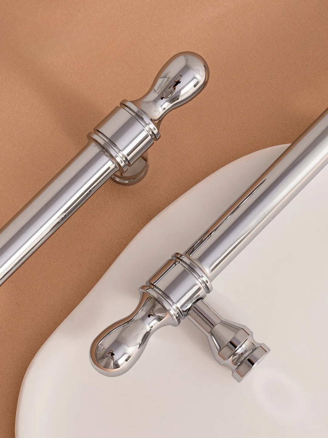 Two chrome curtain rods with decorative finials on a beige and white background