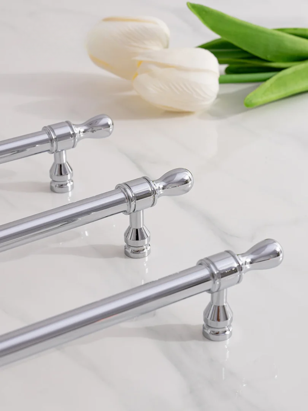 Set of silver cabinet handles on a white surface with tulips in the background