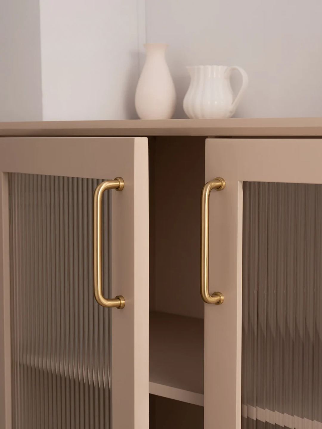 Beige cabinet with gold handles and white decorative items on a light gray background