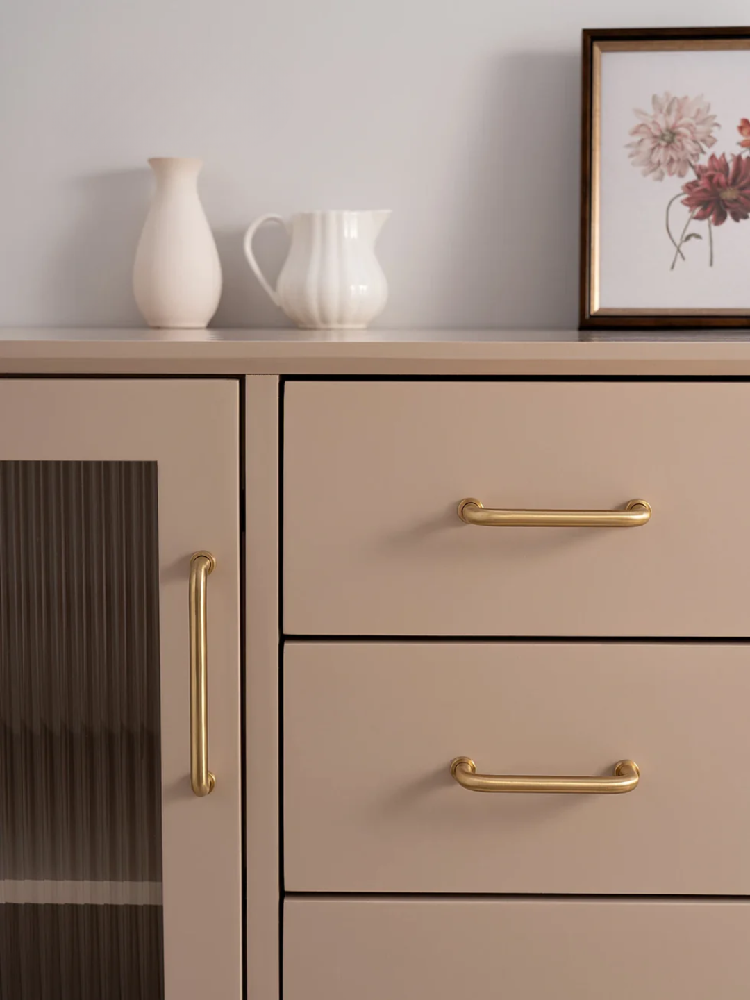 Beige cabinet with gold handles and decorative items on a shelf.