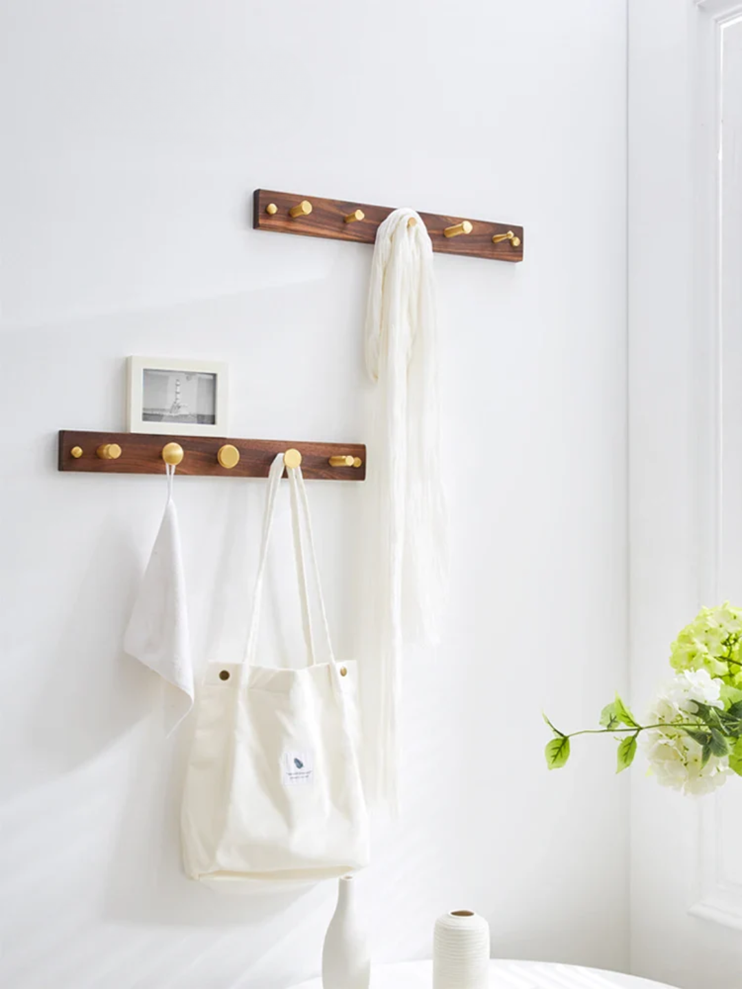 Wooden wall hooks with white bags and a plant on a white wall