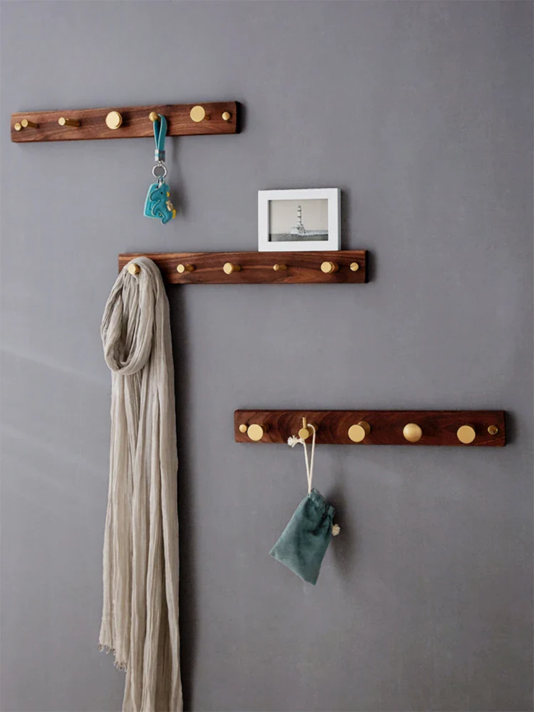 Wooden wall hooks with scarves and a picture frame on a gray wall