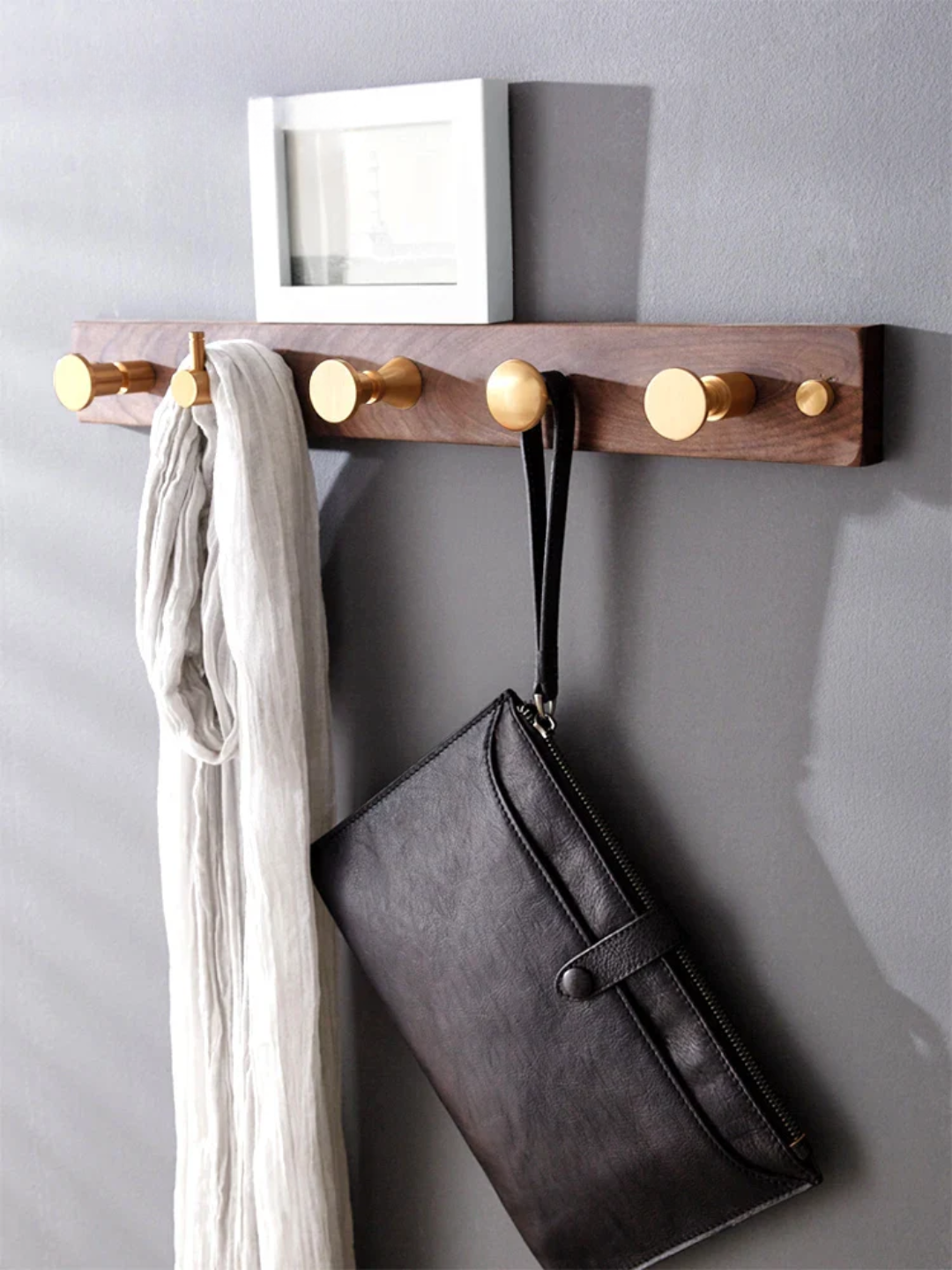 Wooden wall hook with gold knobs holding a scarf and a bag against a gray wall.