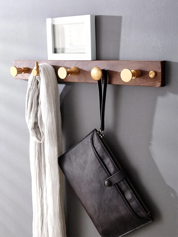 Wooden wall hook with gold knobs holding a scarf and a bag against a gray wall.