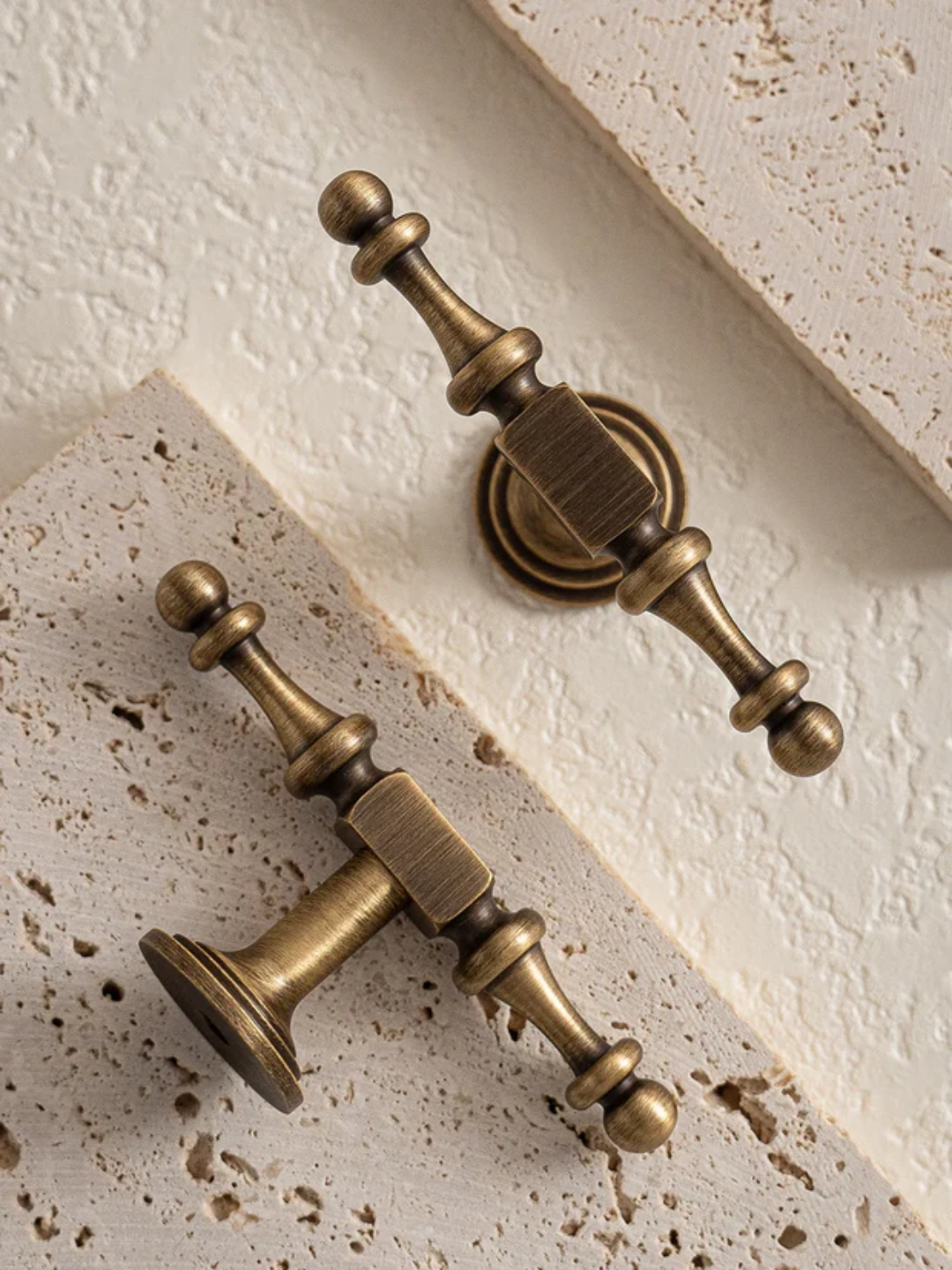 Pair of vintage-style bronze cabinet handles on a textured surface.