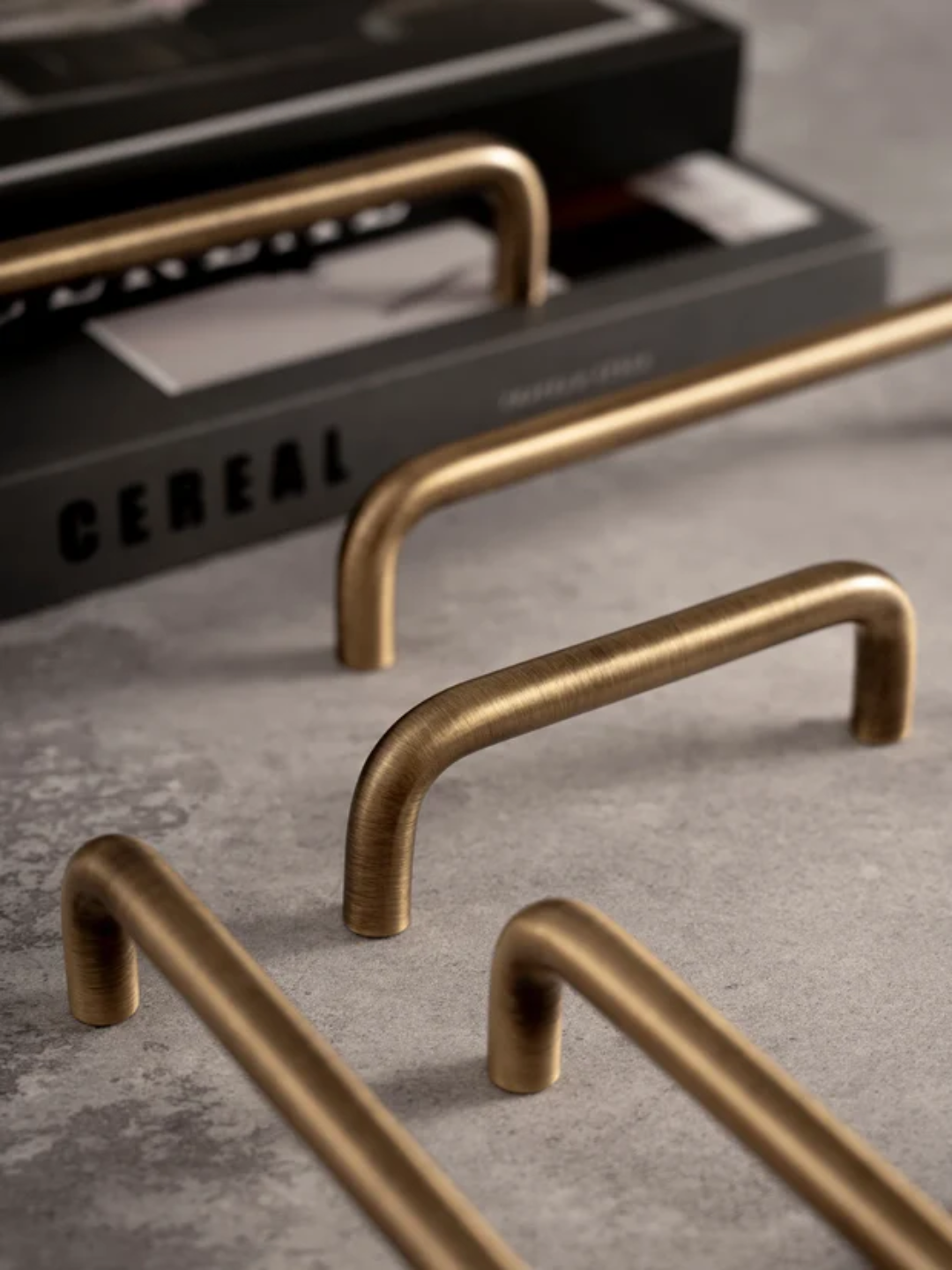Bronze cabinet handles on a concrete surface with a cereal box in the background.