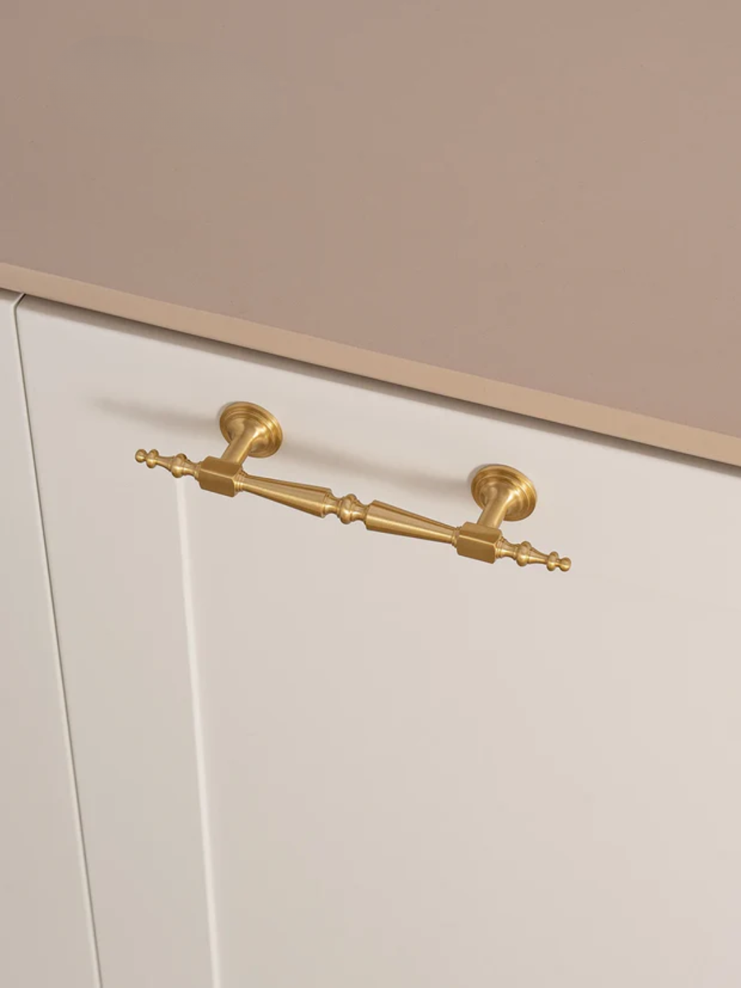 Close-up of a gold cabinet handle on a white cabinet with a beige background