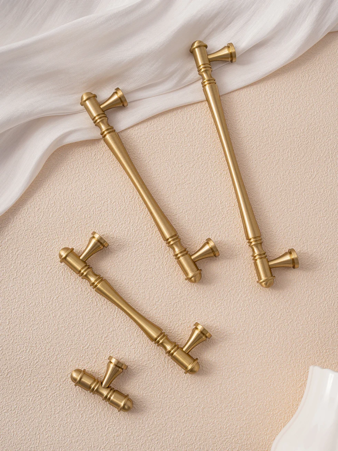 Set of gold kitchen cabinet handles on a beige surface with white fabric background