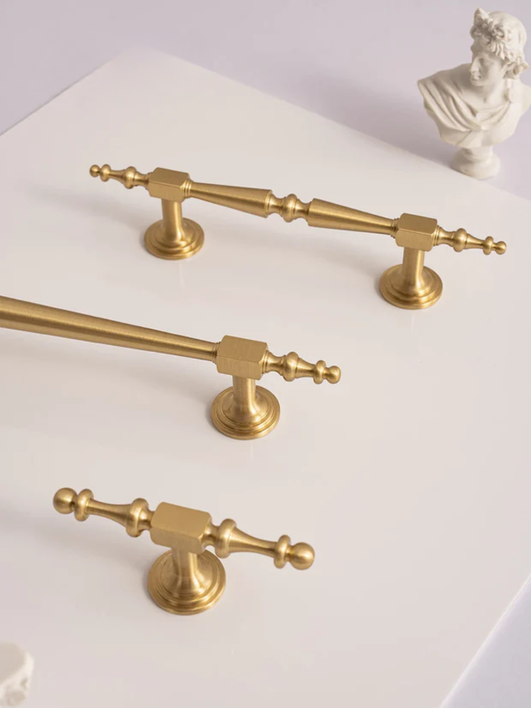 Set of gold bathroom fixtures on a white surface with a small bust in the background.