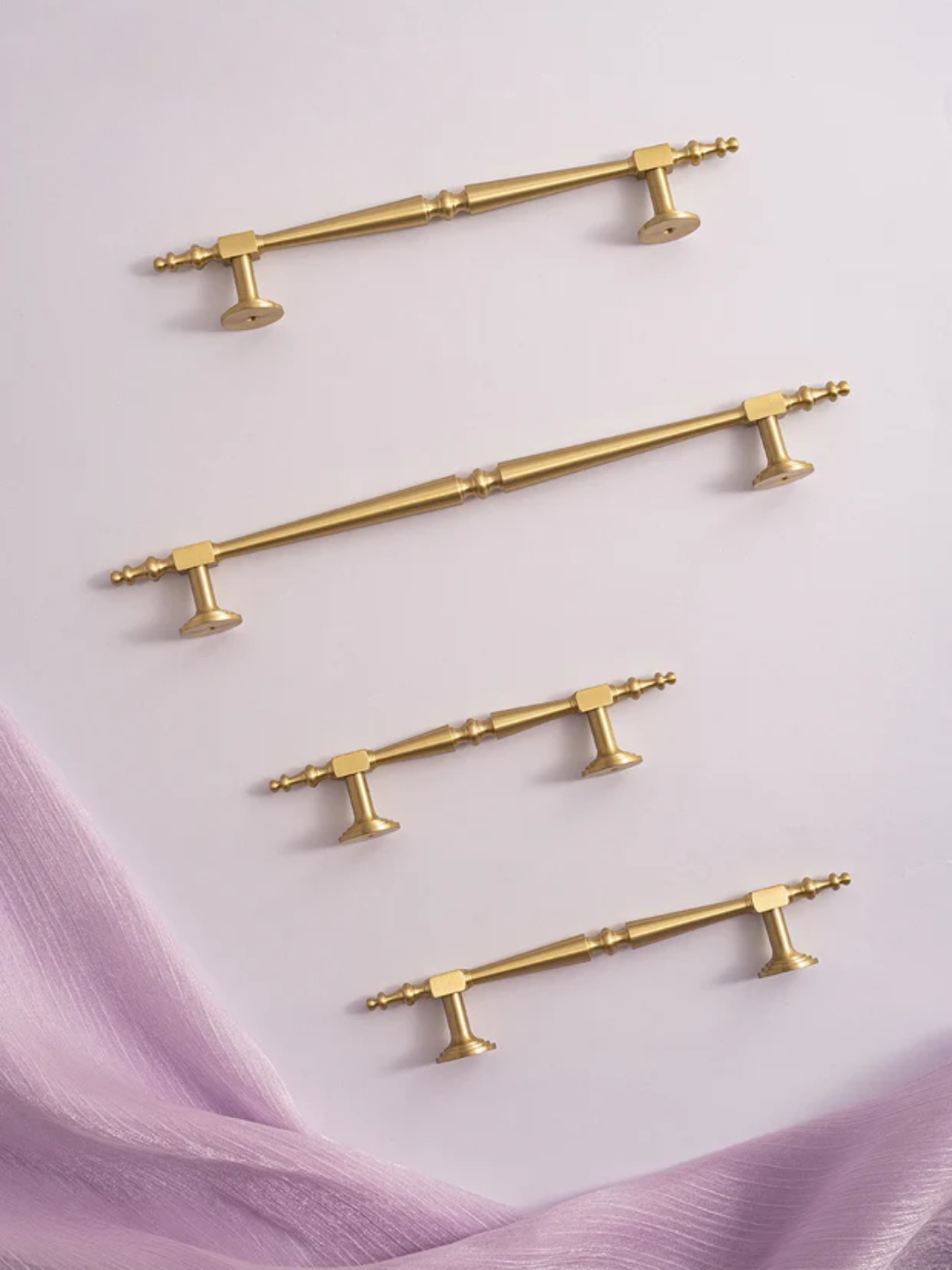 Set of gold cabinet handles on a light purple fabric background