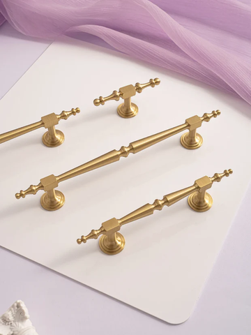 Set of gold cabinet handles on a white surface with purple fabric in the background