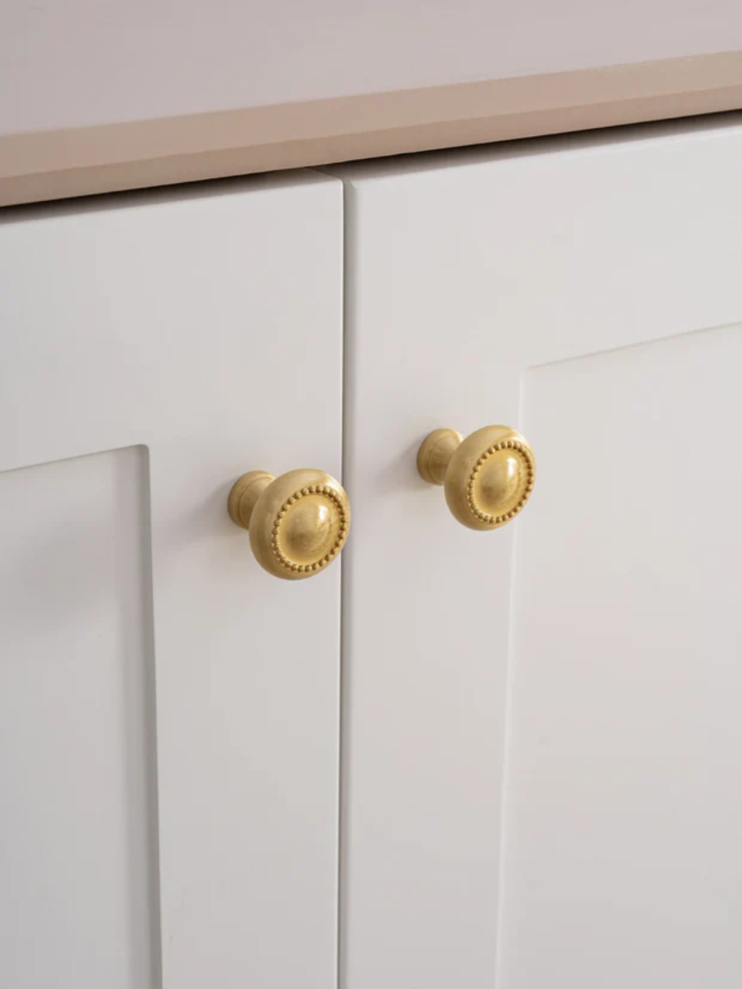 Close-up of white cabinet doors with gold knobs on a neutral background