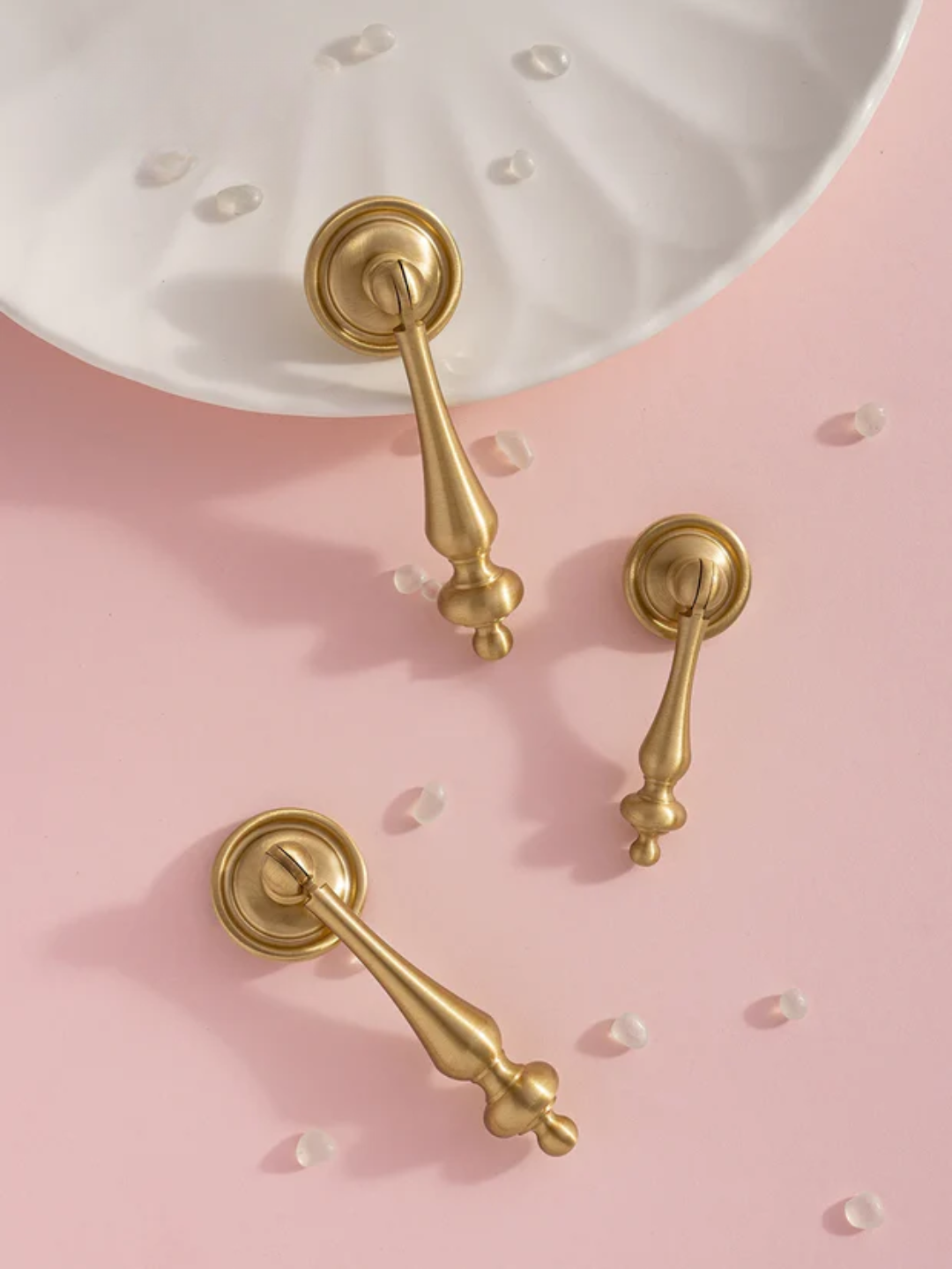 Gold door handles on a pink surface with a white dish in the background