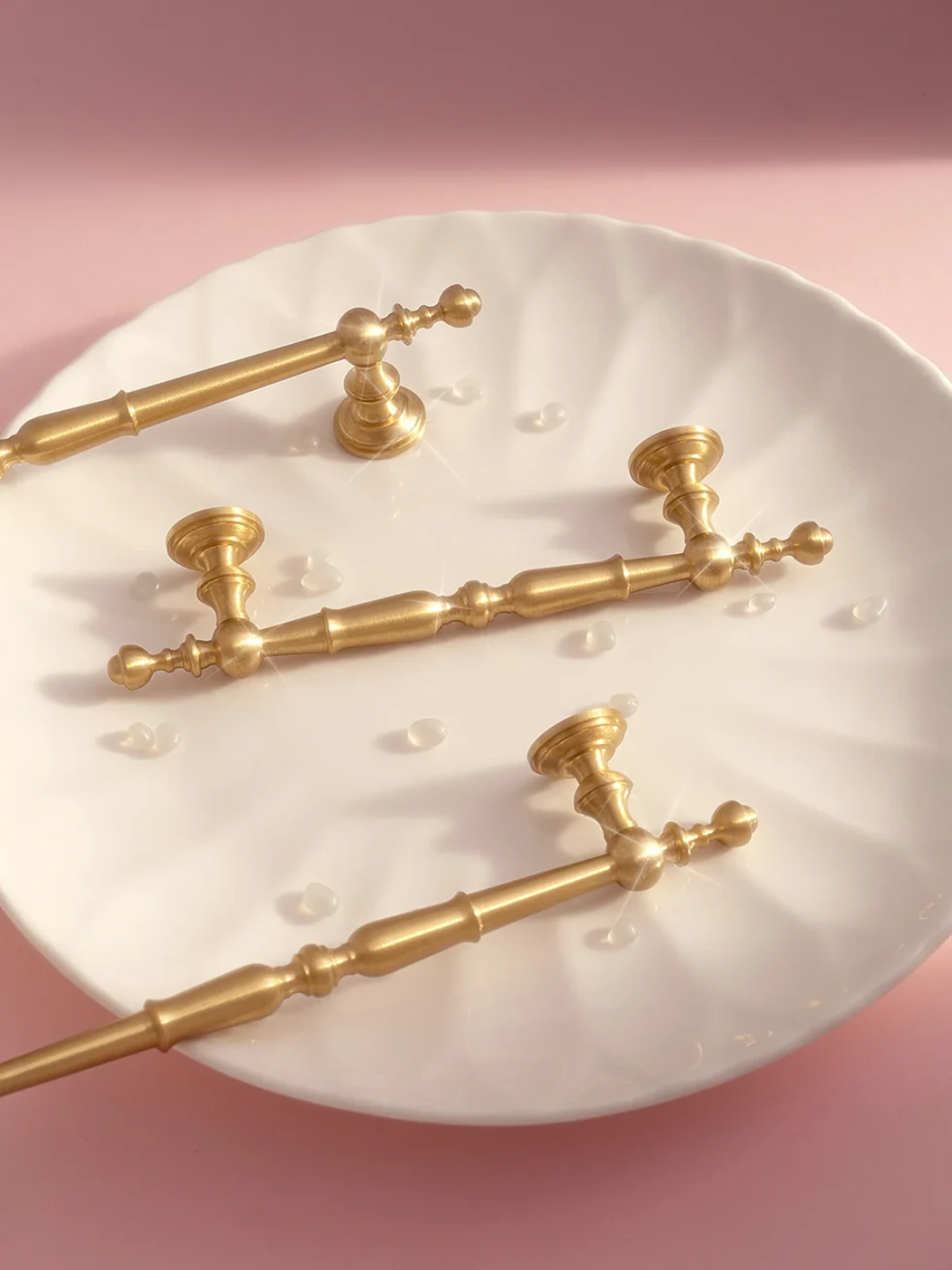 Set of gold door handles on a white plate with a pink background