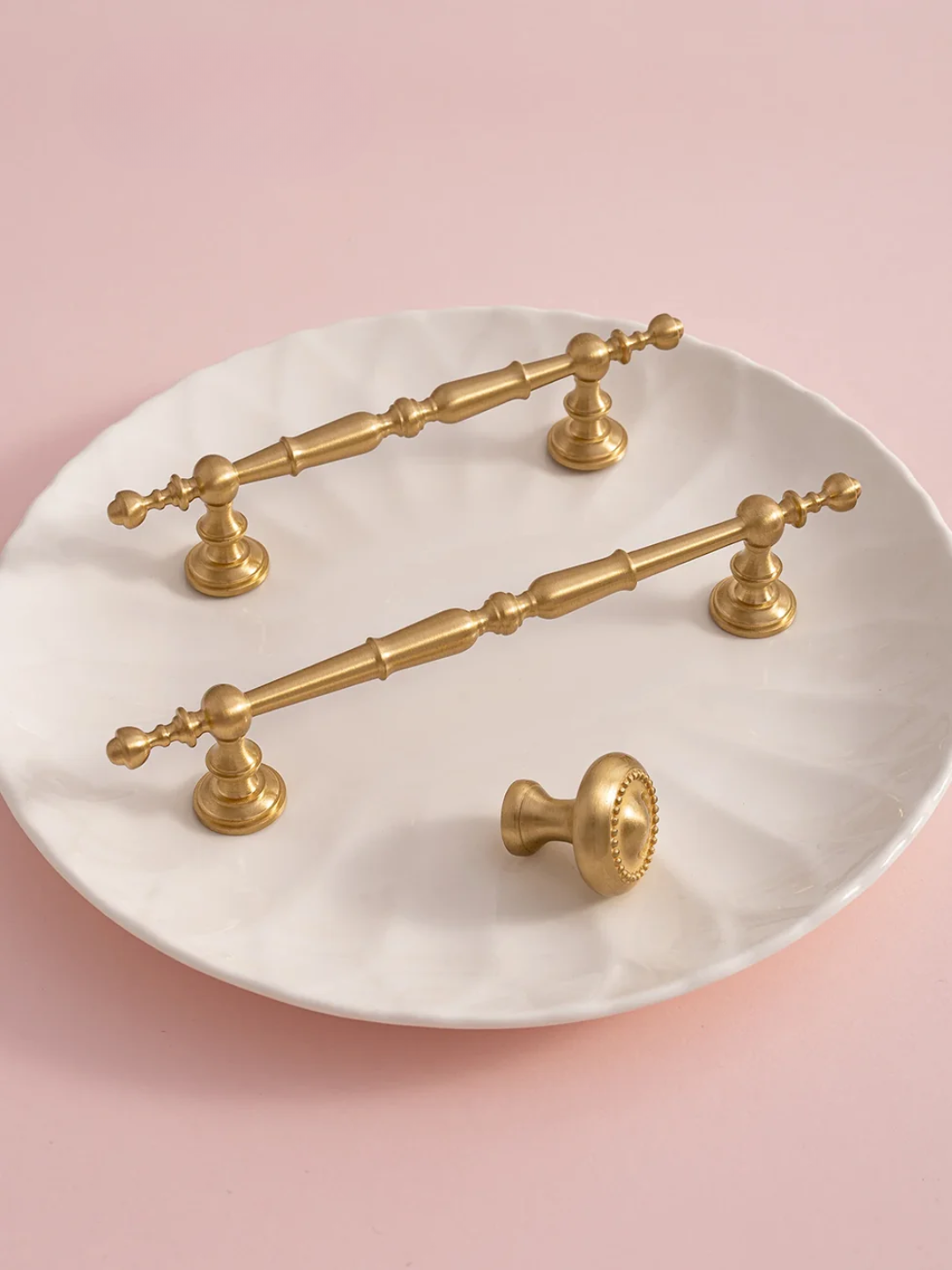 Gold cabinet handles on a white marble tray with a pink background