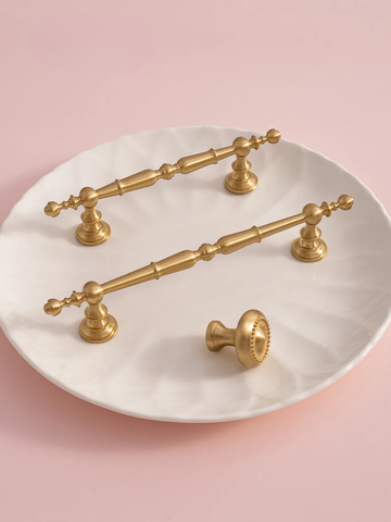 Gold cabinet handles on a white marble tray with a pink background